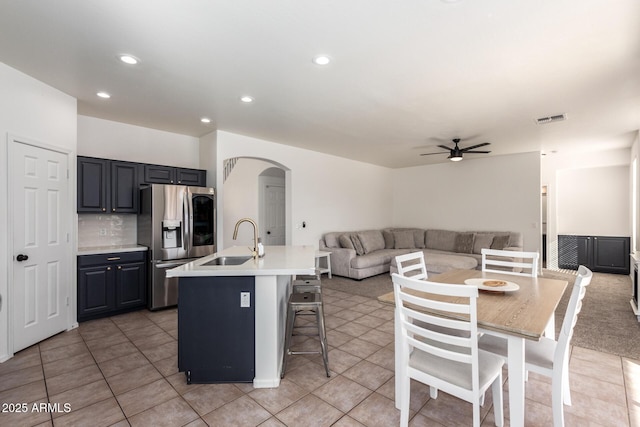 kitchen with a kitchen island with sink, a sink, open floor plan, light countertops, and stainless steel refrigerator with ice dispenser