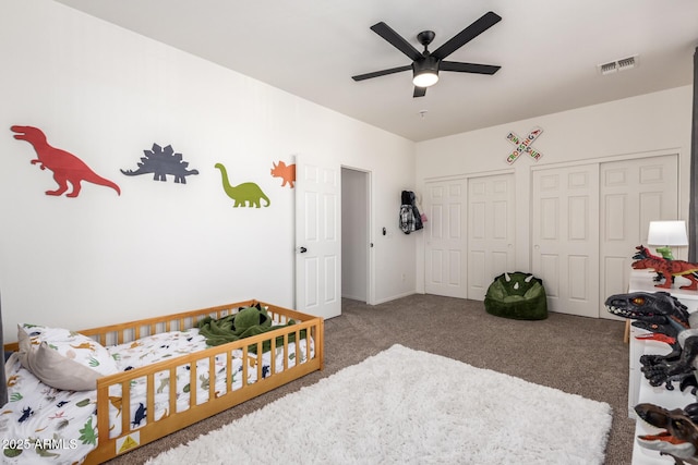 bedroom with carpet, two closets, visible vents, and a ceiling fan