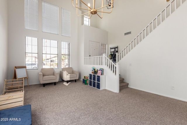 sitting room featuring a chandelier, carpet floors, a towering ceiling, baseboards, and stairs