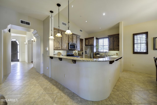 kitchen with a breakfast bar, stainless steel appliances, light stone counters, decorative light fixtures, and kitchen peninsula