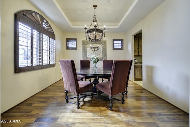 dining space featuring a raised ceiling, hardwood / wood-style flooring, and an inviting chandelier