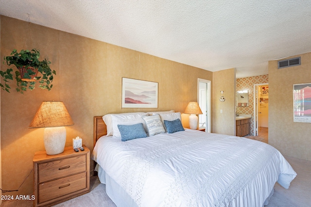 bedroom featuring connected bathroom, a textured ceiling, and light carpet