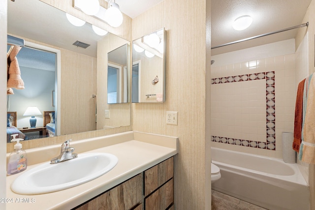 full bathroom featuring toilet, tiled shower / bath combo, vanity, and a textured ceiling