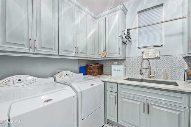 clothes washing area with washing machine and dryer, cabinets, and sink