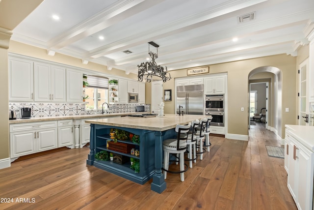 kitchen with backsplash, built in appliances, white cabinetry, and a center island with sink