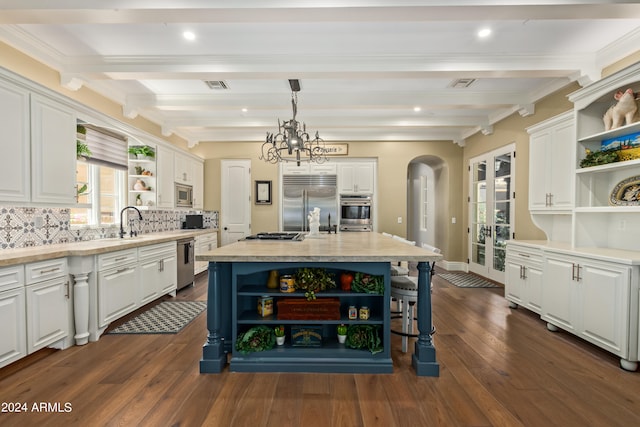 kitchen with a center island with sink, decorative backsplash, built in appliances, hanging light fixtures, and white cabinets