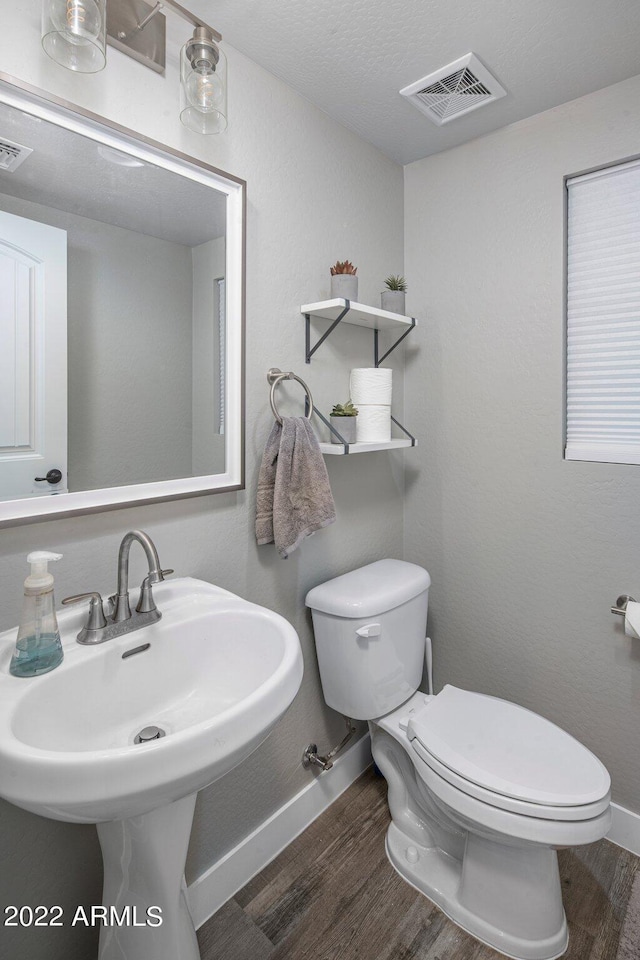 bathroom featuring toilet, wood finished floors, visible vents, and a sink