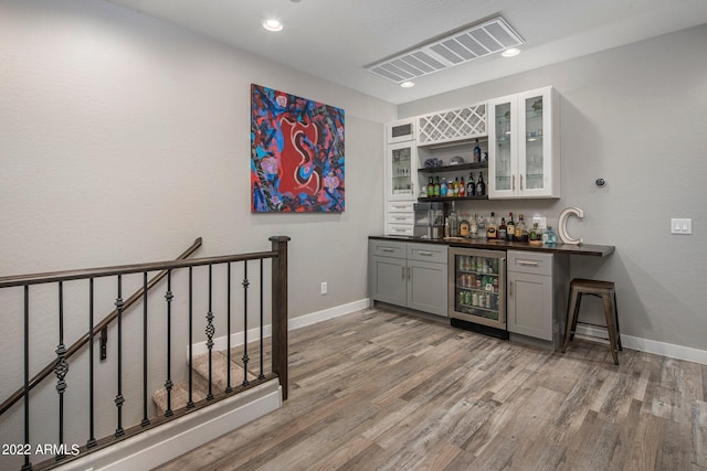 bar with wine cooler, baseboards, a bar, and light wood-style floors