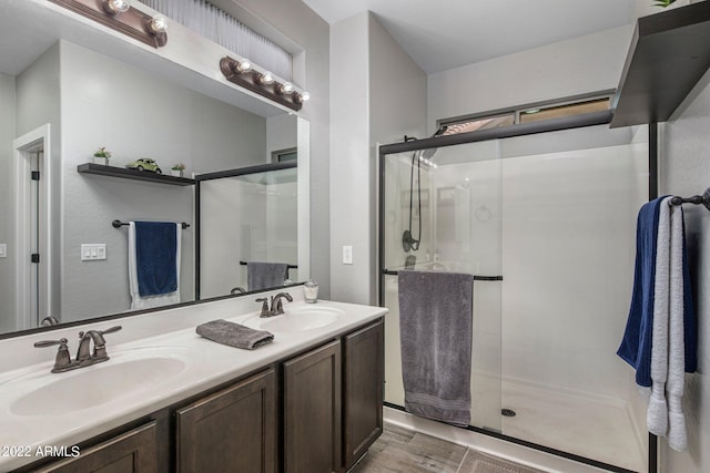 bathroom featuring double vanity, a shower stall, wood finished floors, and a sink