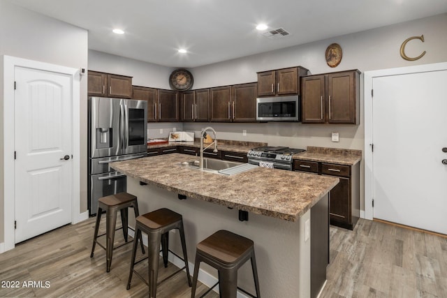 kitchen with a breakfast bar area, visible vents, a sink, dark brown cabinets, and appliances with stainless steel finishes