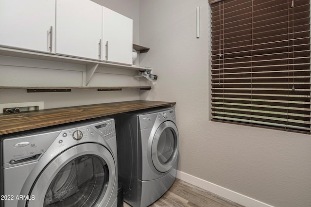 washroom with cabinet space, light wood-style floors, baseboards, washing machine and clothes dryer, and a textured wall