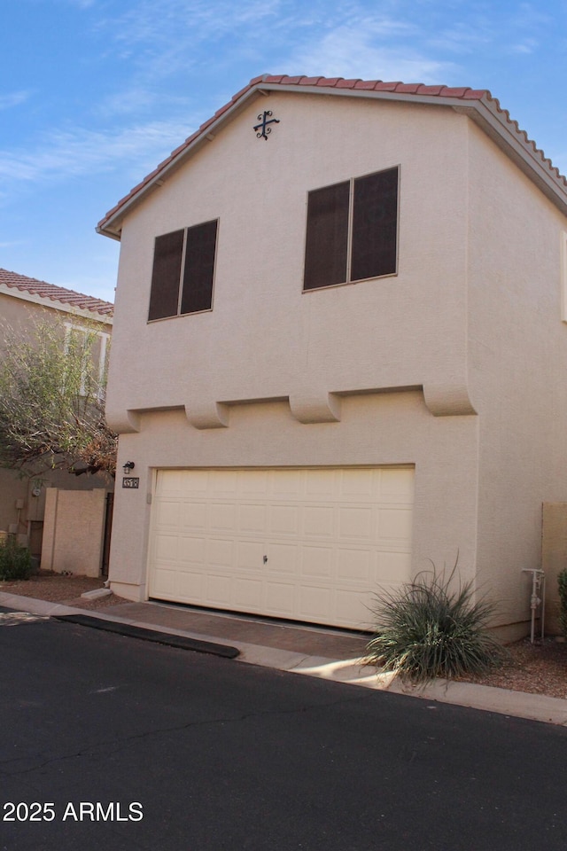 view of front facade with stucco siding, an attached garage, and a tile roof