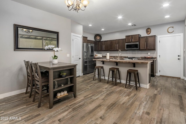 kitchen featuring a kitchen bar, a kitchen island with sink, wood finished floors, stainless steel appliances, and dark brown cabinets