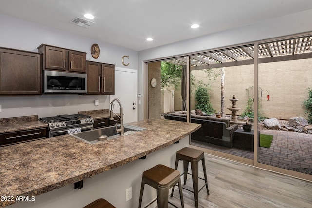 kitchen featuring visible vents, a sink, stainless steel appliances, dark brown cabinetry, and a kitchen breakfast bar