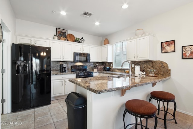 kitchen with sink, black appliances, kitchen peninsula, white cabinets, and dark stone counters