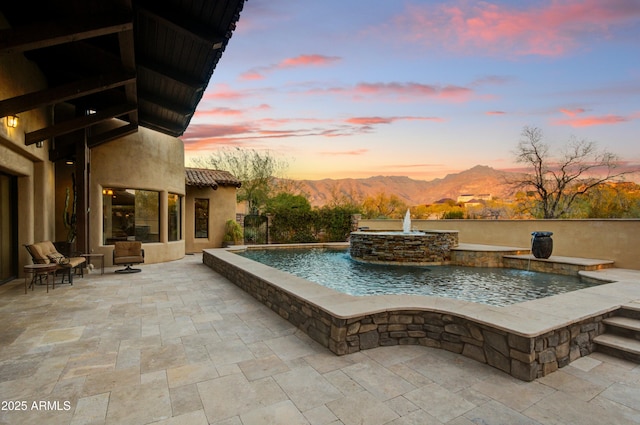 pool at dusk with pool water feature and a mountain view