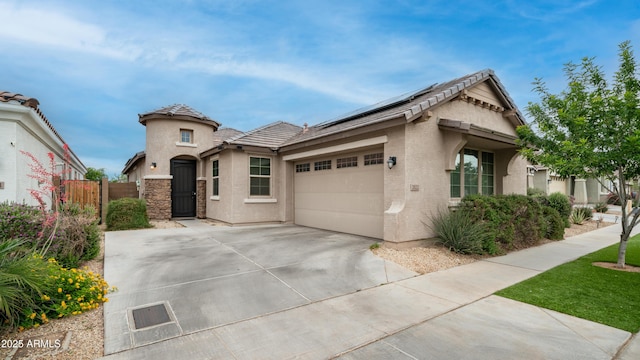 view of front of home featuring stucco siding, concrete driveway, solar panels, a garage, and a gate