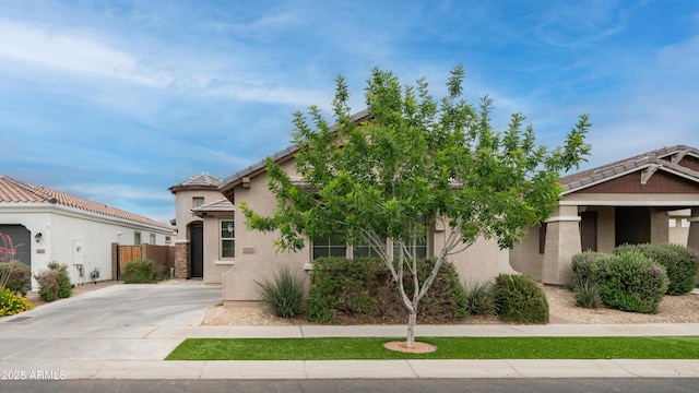 view of front facade featuring a tile roof, driveway, stucco siding, and fence