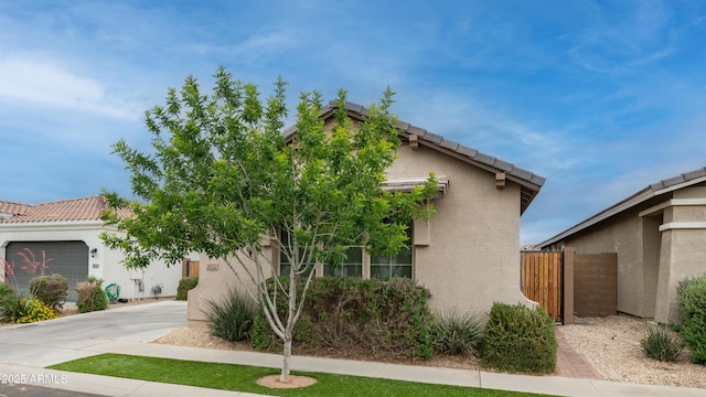 view of front of property with stucco siding, driveway, fence, and a tile roof
