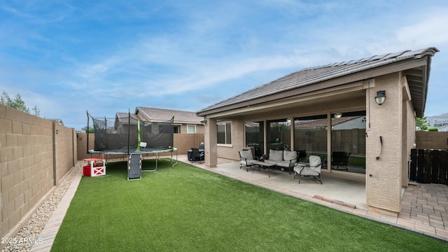 back of property featuring a trampoline, a patio, stucco siding, and an outdoor hangout area