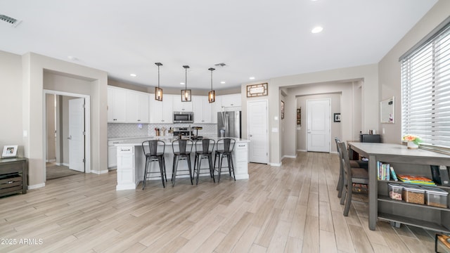 kitchen featuring appliances with stainless steel finishes, white cabinets, light countertops, a breakfast bar area, and backsplash
