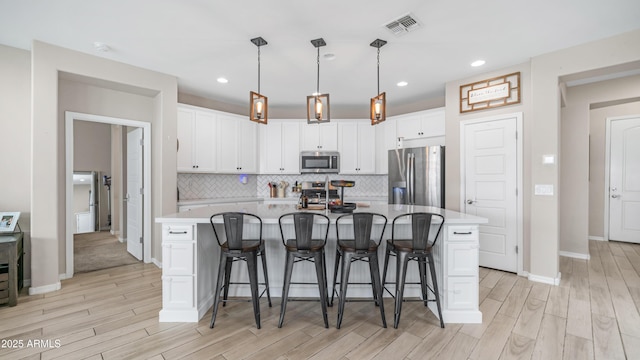 kitchen with stainless steel appliances, light wood finished floors, white cabinetry, backsplash, and recessed lighting