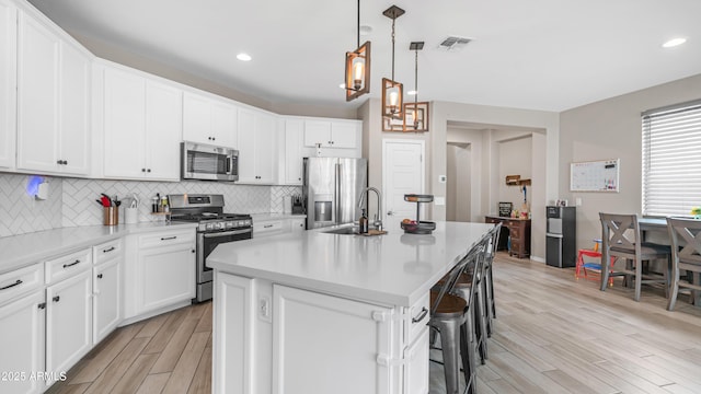 kitchen featuring stainless steel appliances, light wood-type flooring, a sink, a kitchen breakfast bar, and tasteful backsplash