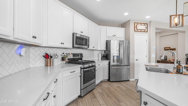 kitchen featuring appliances with stainless steel finishes, a sink, light countertops, white cabinetry, and pendant lighting