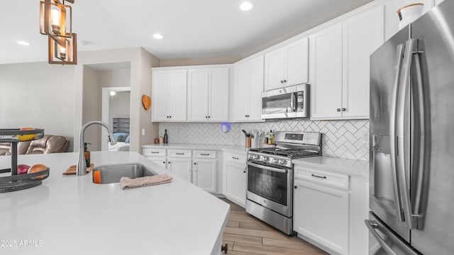 kitchen with stainless steel appliances, a sink, light wood-style flooring, light countertops, and decorative backsplash