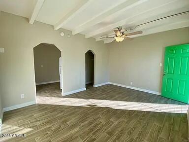 1620 E Palm Ln, Phoenix, AZ 85006 - empty room with beam ceiling, arched walkways, ceiling fan, dark wood-type flooring, and baseboards