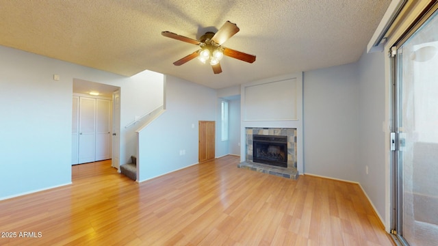 unfurnished living room featuring light wood-style flooring, stairs, ceiling fan, and a stone fireplace