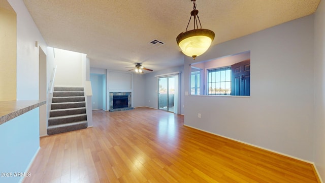 unfurnished living room with a textured ceiling, light wood-style flooring, a fireplace, visible vents, and stairway