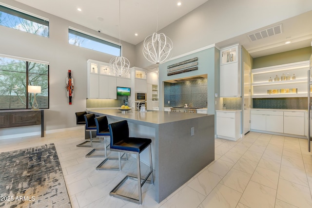 kitchen featuring backsplash, a towering ceiling, white cabinets, and a notable chandelier