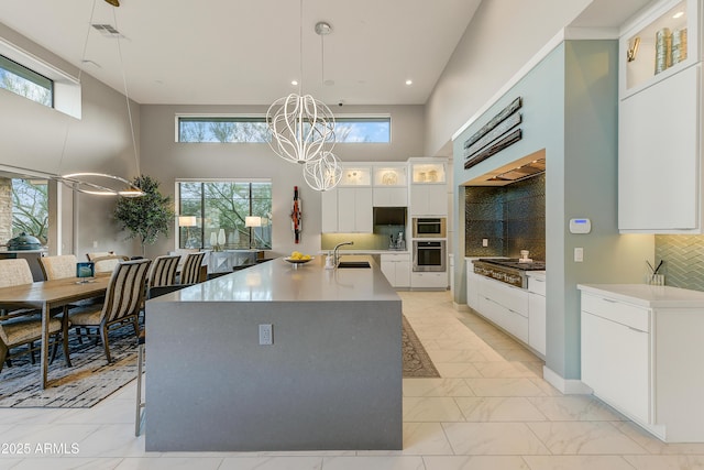 kitchen with backsplash, hanging light fixtures, white cabinetry, stainless steel appliances, and a chandelier