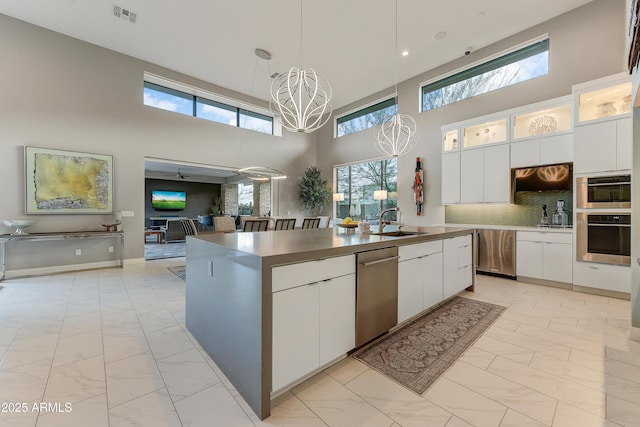 kitchen with backsplash, sink, pendant lighting, a center island with sink, and white cabinetry