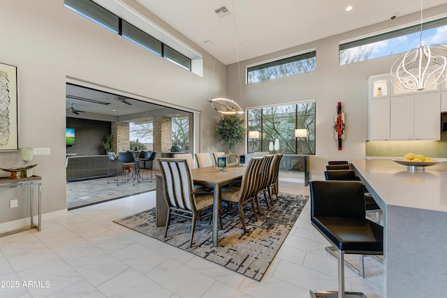 dining space featuring ceiling fan with notable chandelier, a towering ceiling, and a wealth of natural light