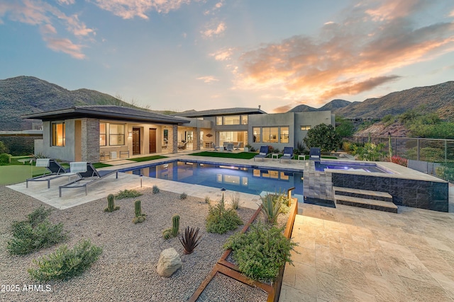 pool at dusk with a patio area, an in ground hot tub, and a mountain view