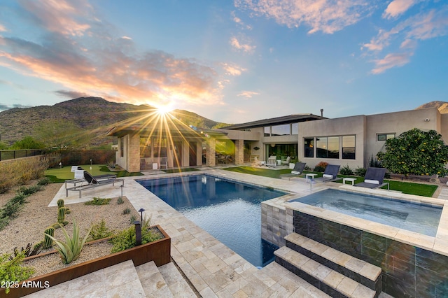 pool at dusk with a mountain view, a patio, and an in ground hot tub