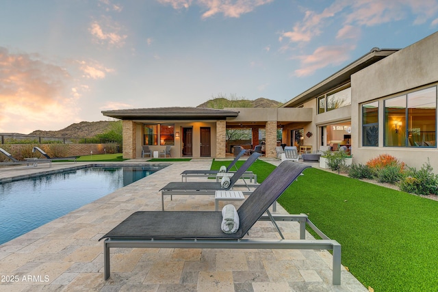 pool at dusk with a mountain view, a patio, and a lawn