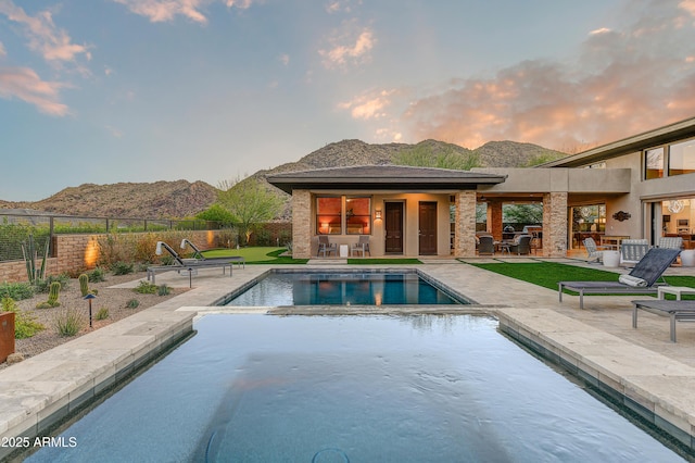 pool at dusk featuring a mountain view, a jacuzzi, a patio, and exterior kitchen