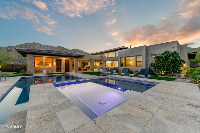 pool at dusk featuring a patio area, a mountain view, and a hot tub