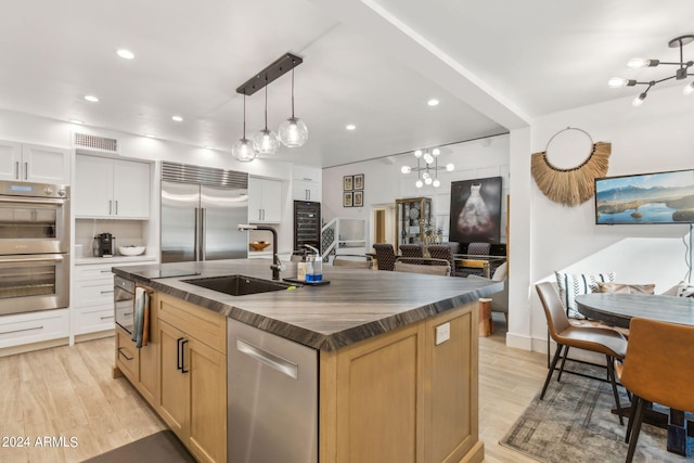 kitchen featuring decorative light fixtures, sink, white cabinetry, a kitchen island with sink, and appliances with stainless steel finishes