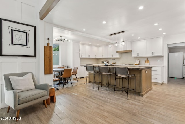 kitchen with decorative light fixtures, white cabinetry, white refrigerator, and a kitchen island with sink