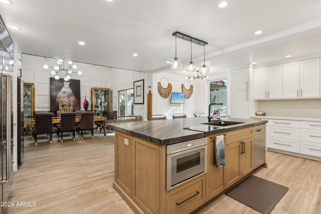 kitchen with white cabinetry, light hardwood / wood-style flooring, hanging light fixtures, and a kitchen island with sink