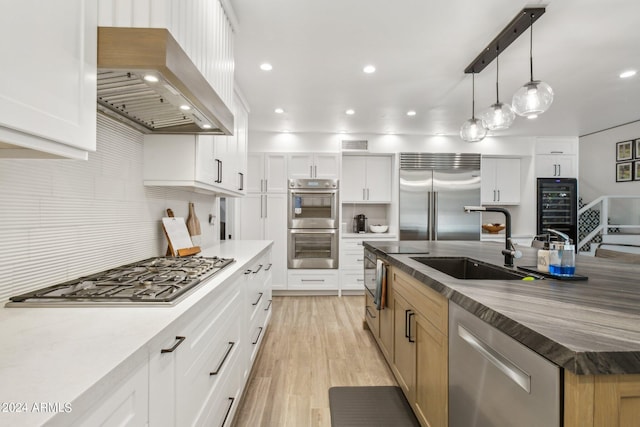 kitchen with exhaust hood, pendant lighting, sink, white cabinetry, and stainless steel appliances