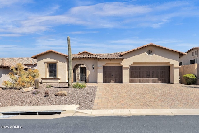 mediterranean / spanish-style home with a tiled roof, a garage, stucco siding, and decorative driveway