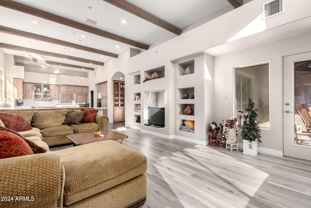 living room featuring beamed ceiling, built in features, and light hardwood / wood-style flooring