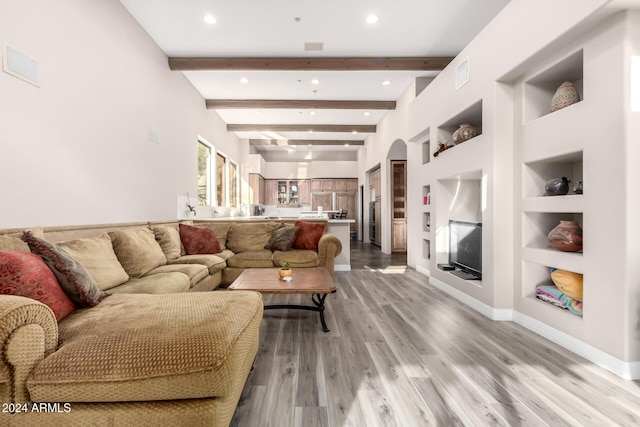 living room featuring beamed ceiling, light wood-type flooring, and built in features