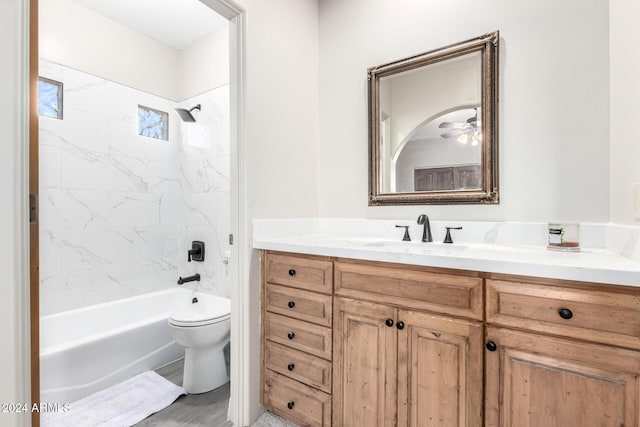 full bathroom featuring tiled shower / bath combo, ceiling fan, toilet, and vanity