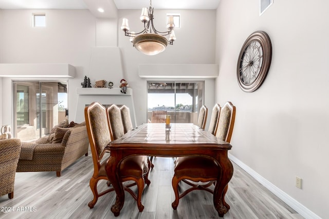 dining room with a towering ceiling, light wood-type flooring, and a notable chandelier